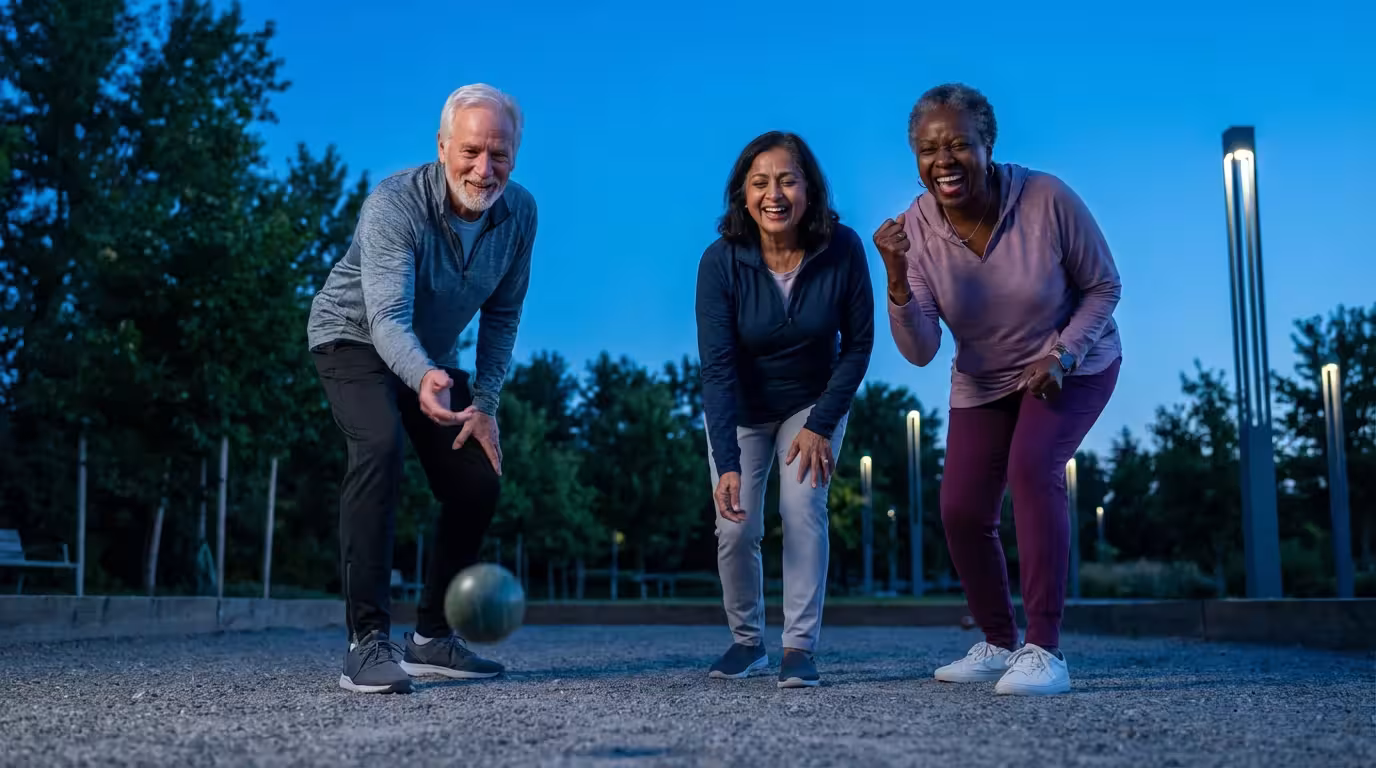 A diverse group of seniors laughing while playing bocce ball in a park at twilight.