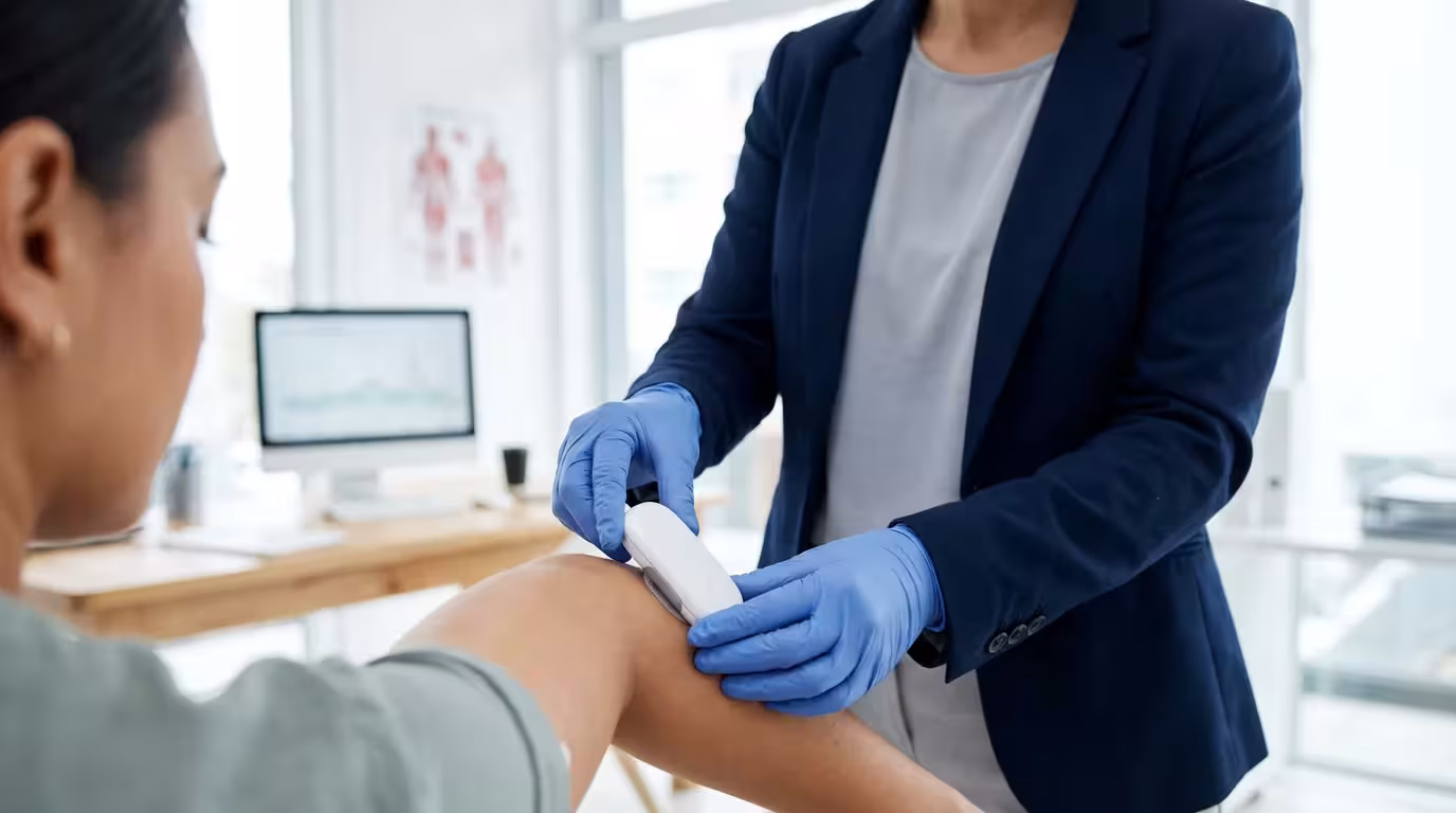 A healthcare professional helps a patient apply a continuous glucose monitor in an office.